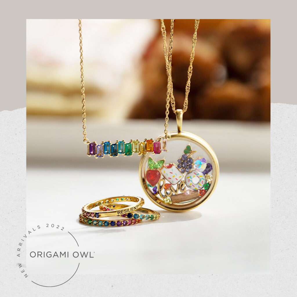 A picture of empowerment rainbow jewelry that shows a gold locket and charms, rainbow baguette necklace and rainbow gold ring that has resilience written on it 