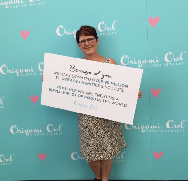 an aqua origami owl back with colleen holding a sign in a printed dress. the sign shows because of you we donated over $5 million dollars