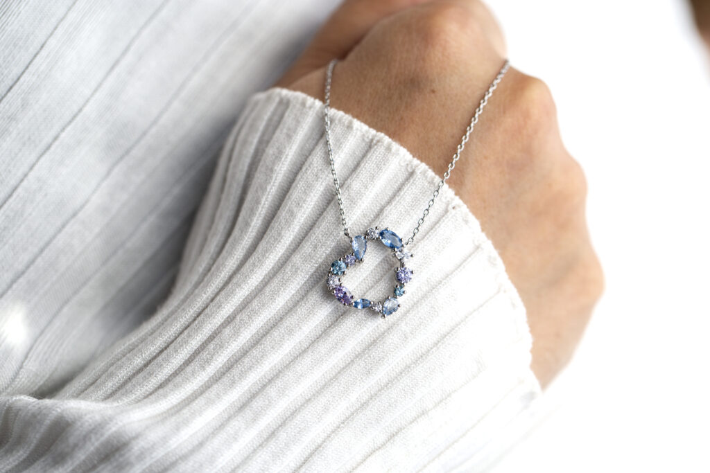 Woman’s hand with white sweater and blue heart pendant 
