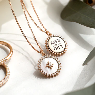 a rose gold empowerment necklace on a chain. the front has a north star and the back says life is a gift