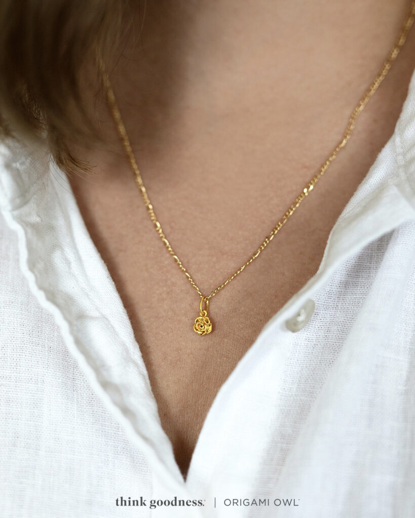 A woman’s neck in a white blouse wearing a gold flower pendant