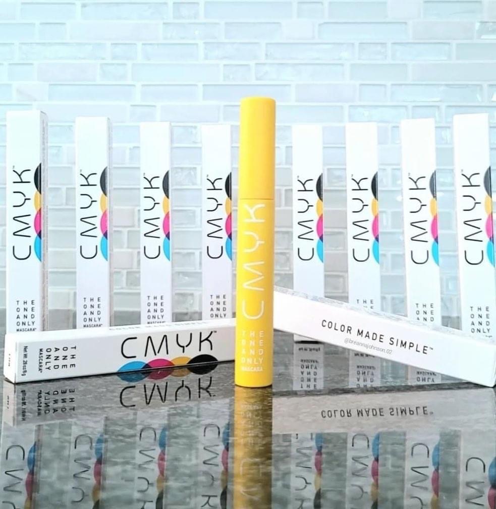 A picture of a yellow tube of CMYK mascara with several mascara boxes in background 