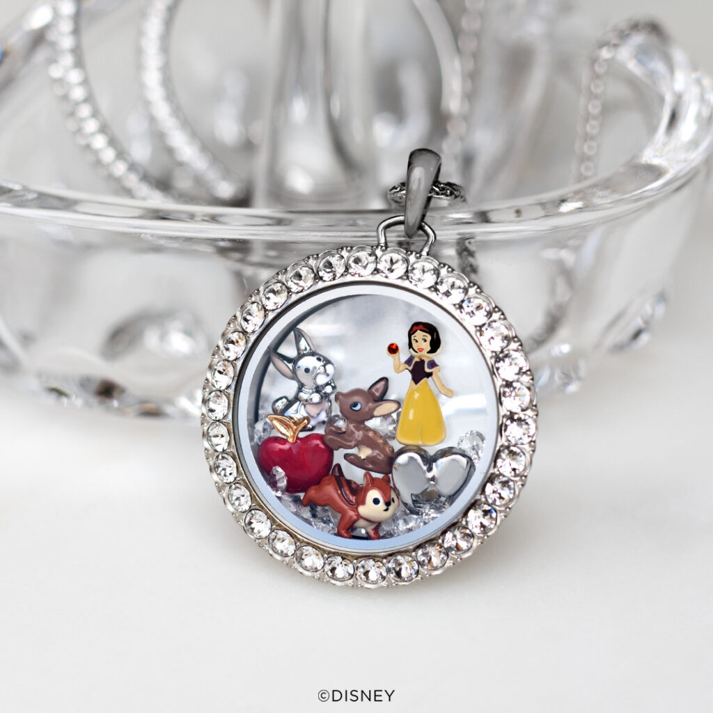A white background with a round living locket and Snow White charms