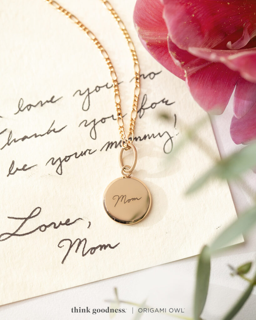 A note that’s handwritten and signed love mom with a rose gold round inscription pendant on a chain that has the handwritten signature on it