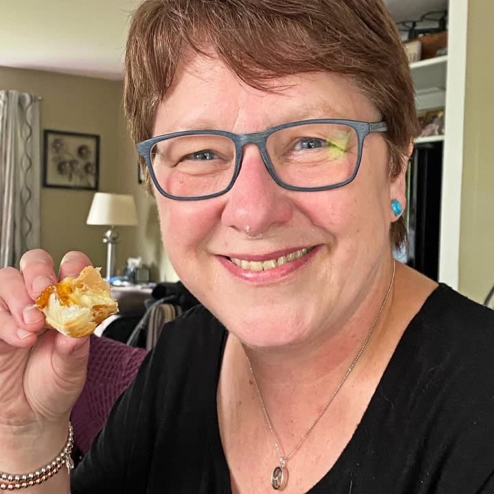 A headshot of Colleen Evans laughing with a cream puff in her hand and some cream on her nose with no makeup and no filter