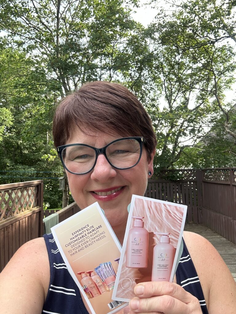 an image of Colleen Evans with trees in the background holding curly and coily shampoo and conditioner samples