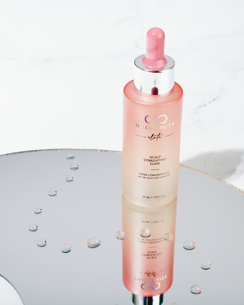 a mirror with a pink bottle of Hairfinity Elite Scalp Stimulating Elixer reflecting in mirror