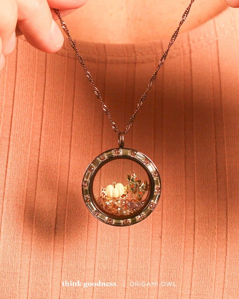 a picture of someone in a peach sweater holding the blushing fall twist living locket set with blushing fall stardust pack, white pumpkin harvest charm and 2 harvest corn charms for fall season 2023