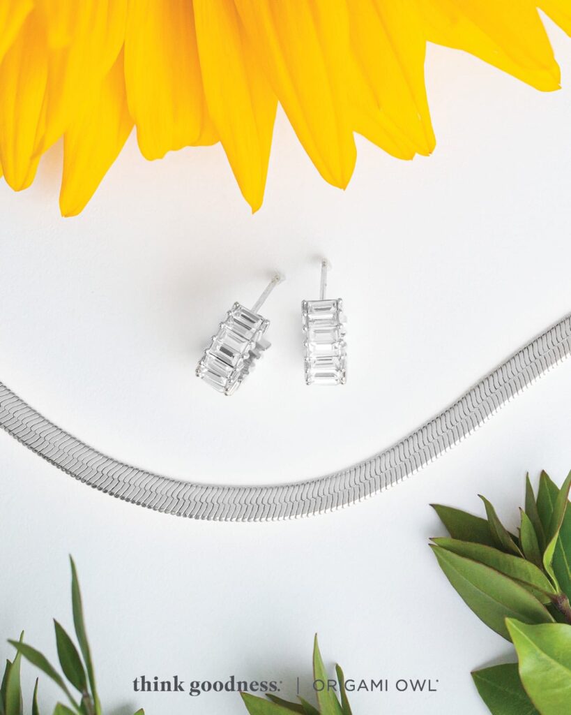  a white background with some green leaves and sunflower petals with the flat snake change and baguette mini hoop earrings