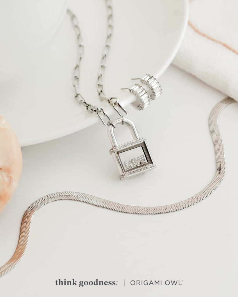 a white background with a white dish showing the flat snake chain, crystal padlock living locket necklace and baguette crystal mini hoop earrings