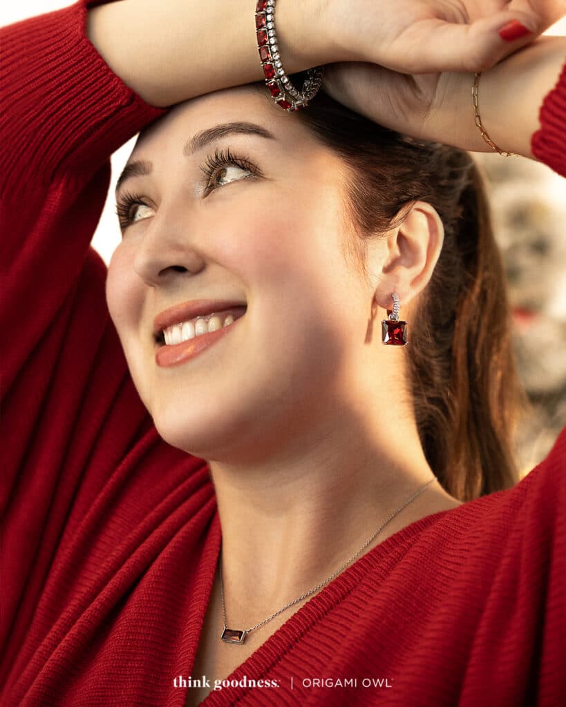 a lady's face in a red v-neck sweater wearing the siam baguette tennis bracelet, fierce baguette pendant necklace and siam drop earrings. all red baguette crystals