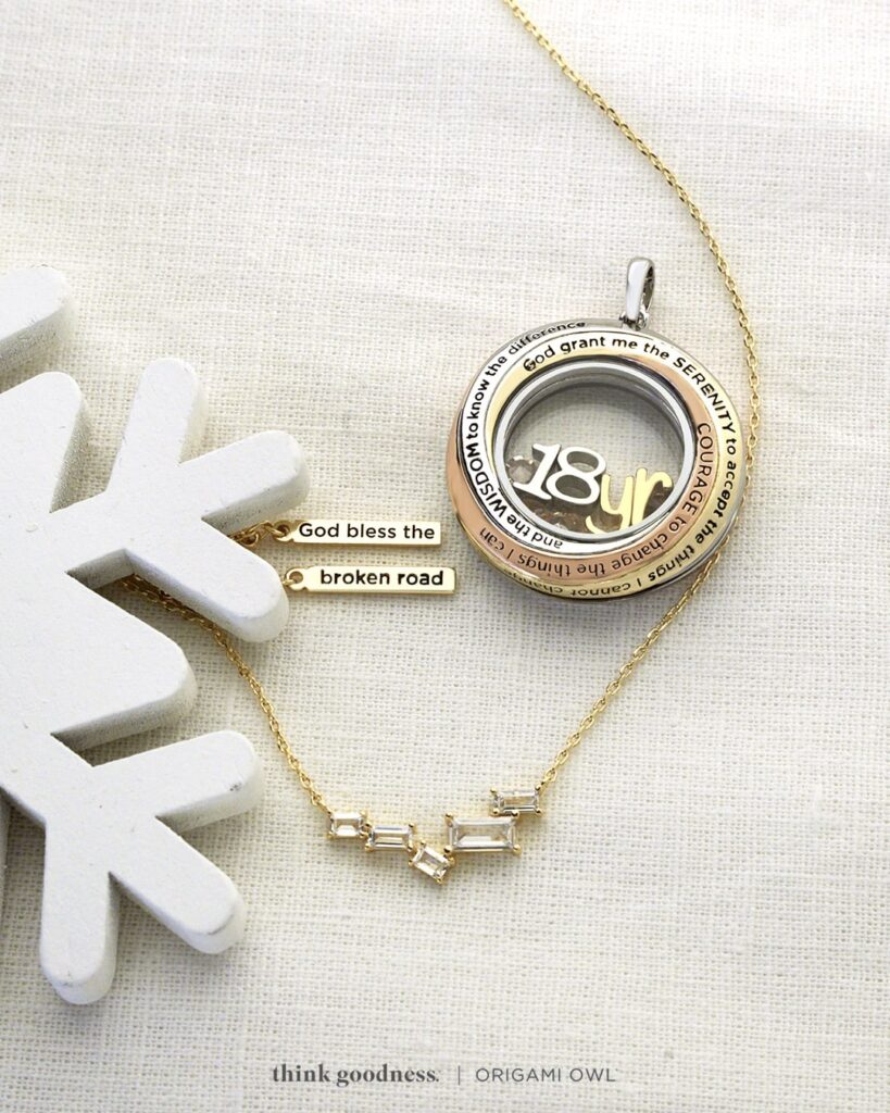 Embrace the spirit of the holiday season with the Gold God Bless the Broken Road Necklace that has 5 clear baguette crystals and the middle one on the showing slanted as a symbol of the broken road and the Medium Tri-Tone Serenity Prayer Living Locket on a light woven fabric with half a snowflake on the left