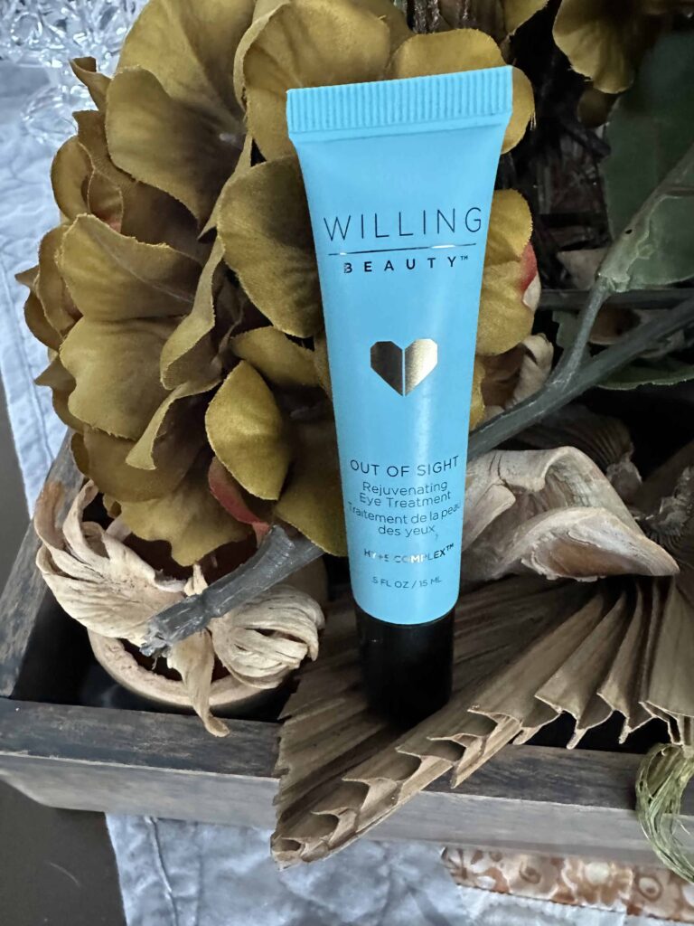 A gold flower background with a blue tube of Willing Beauty’s out of sight rejuvenating eye treatment that is an essential daily Skincare product