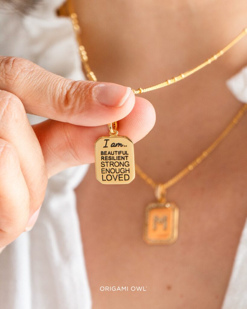 a picture of a woman's neck wearing a white blouse and our gold initial pendant necklace with the letter 'M' and wearing a second one with the back of the initial pendant that says 'I am beautiful, resilient, strong, enough, loved